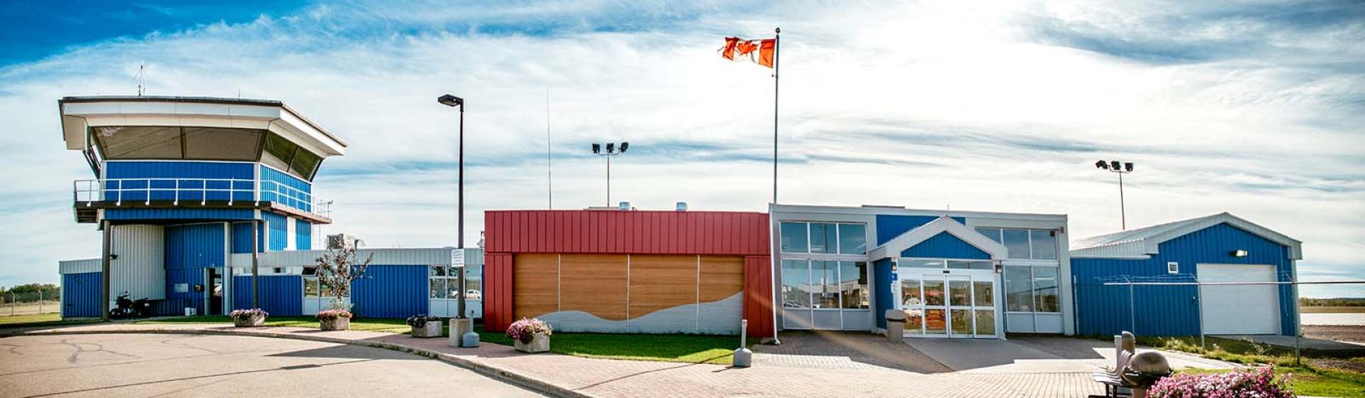 External view of airport building front with blue and red siding, and a Canadian flag at the top of a flagpole.