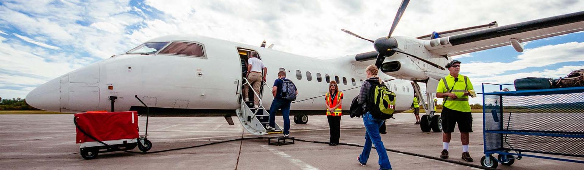 Three people boarding a plane on the tarmac with airport staff standing nearby.
