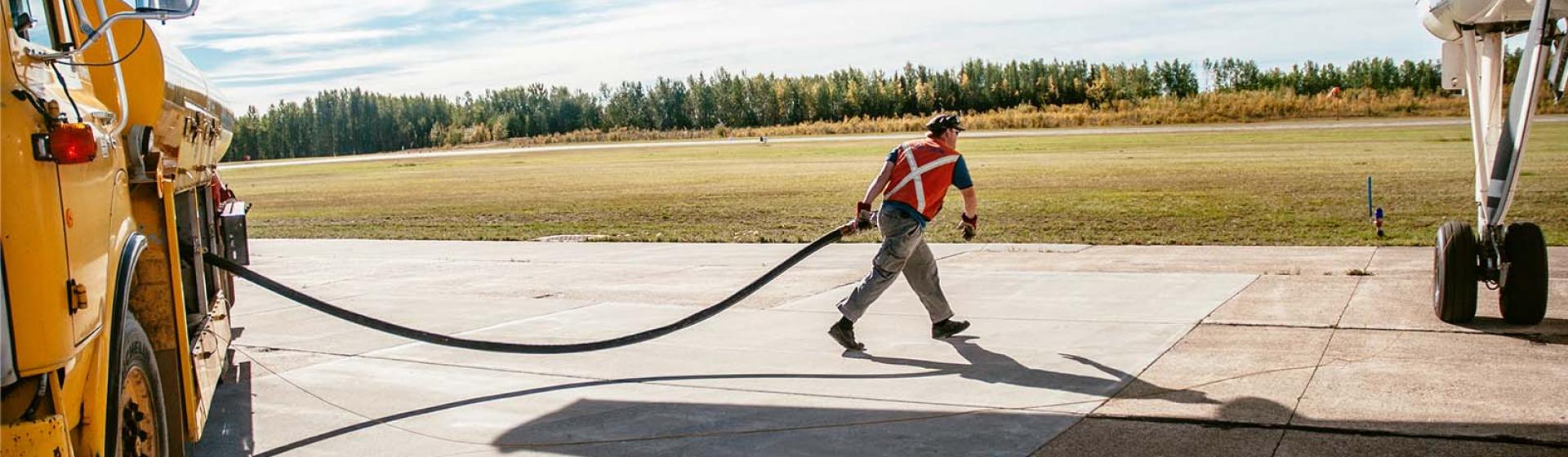 Airport worker on the tarmac walking and holding a fuel line