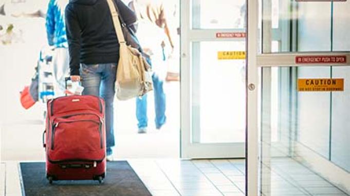 Person rolling a red suitcase into open doors of the airport